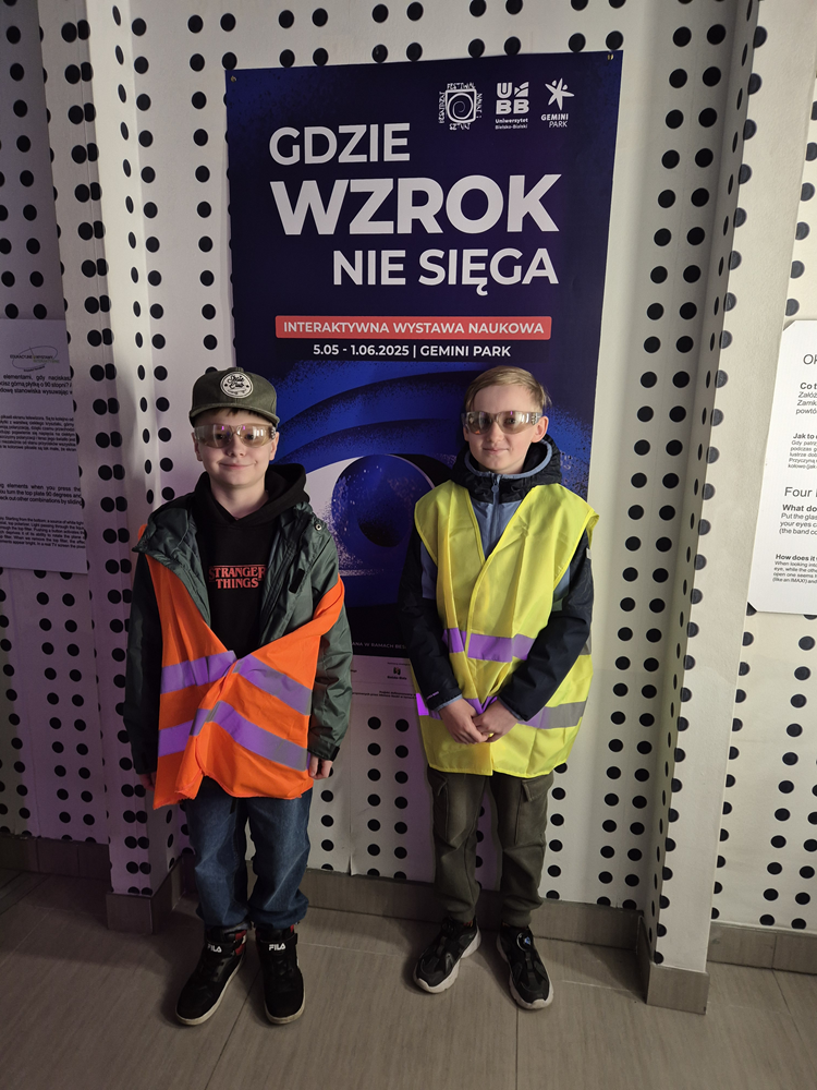 Uczniowie pozują przy plakacie wystawy "Gdzie wzrok nie sięga"