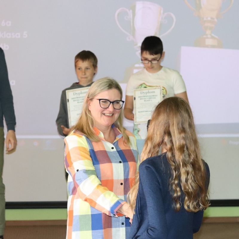 3 uczniów stoi na scenie dyrektor wręcza dyplom uczennicy