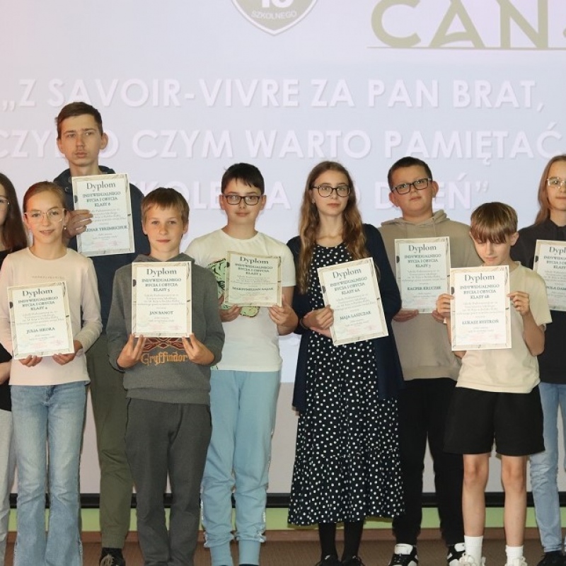 Uczniowie na scenie z dyplomami w ręce z nauczycielem