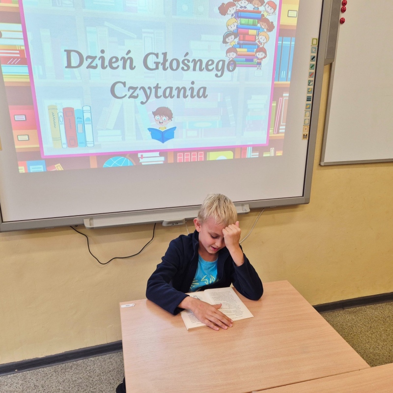 Uczeń klasy 4b czytający książkę na tle napisu na tablicy