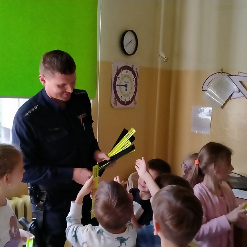 Pan policjant rozdaje uczniom opaski odlblaskowe