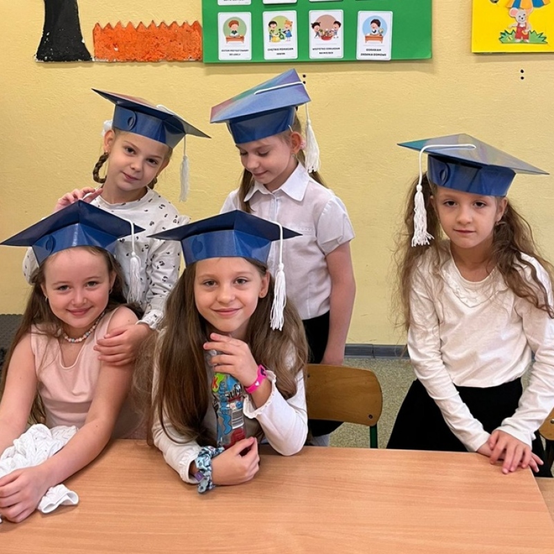 5 dziewczynek siedzi w ławce w biretach