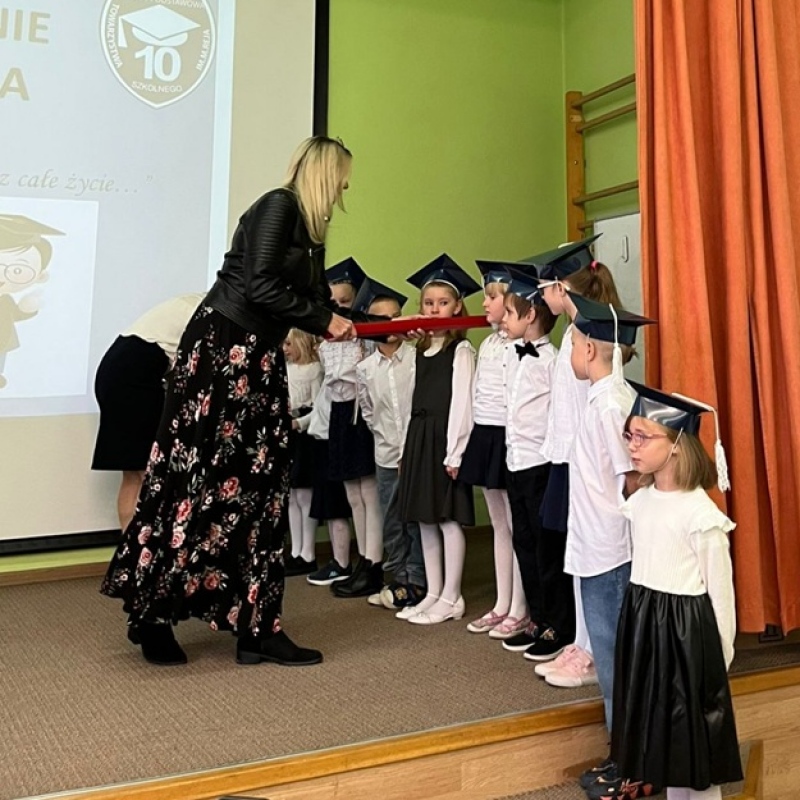 pani dyrektor pasuje na uczniów dzieci stojące na scenie