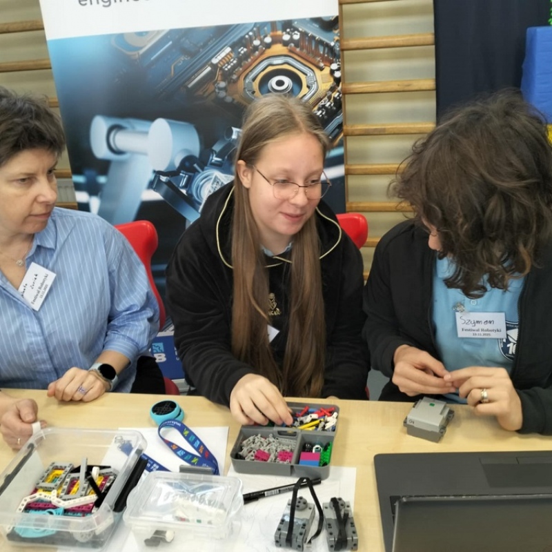 nauczyciel z uczniami siedzi przy laptopie i budują konstrukcję z lego