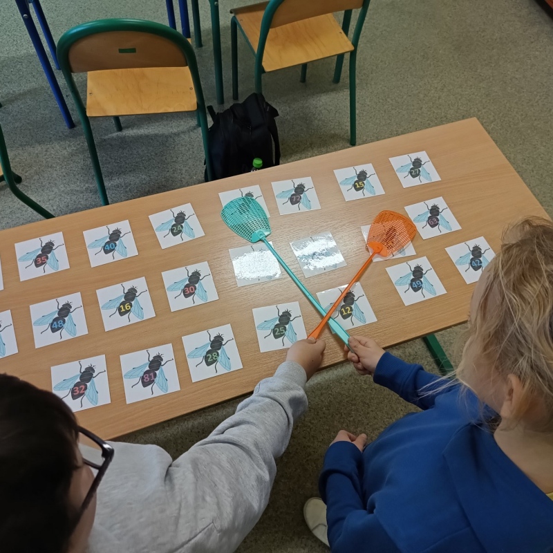 Uczniowie grający w "muchy" - na stoliku obrazki much z liczbami