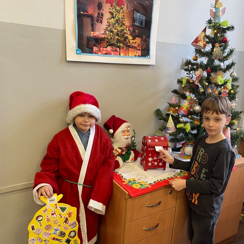 Uczniowie przy skrzynce na listy do Mikołaja w sali i choince jeden uczeń w stroju Mikołaja