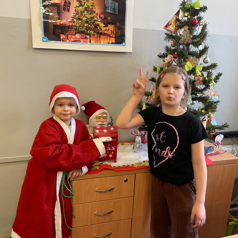 Uczniowie przy skrzynce na listy do Mikołaja w sali i choince jeden uczeń w stroju Mikołaja