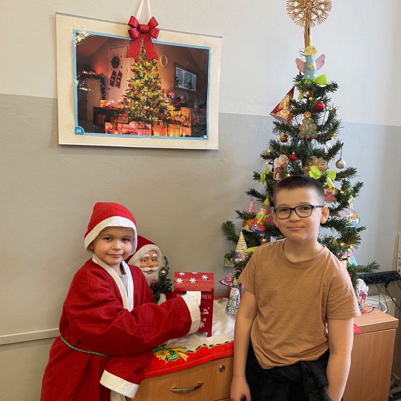 Uczniowie przy skrzynce na listy do Mikołaja w sali i choince jeden uczeń w stroju Mikołaja