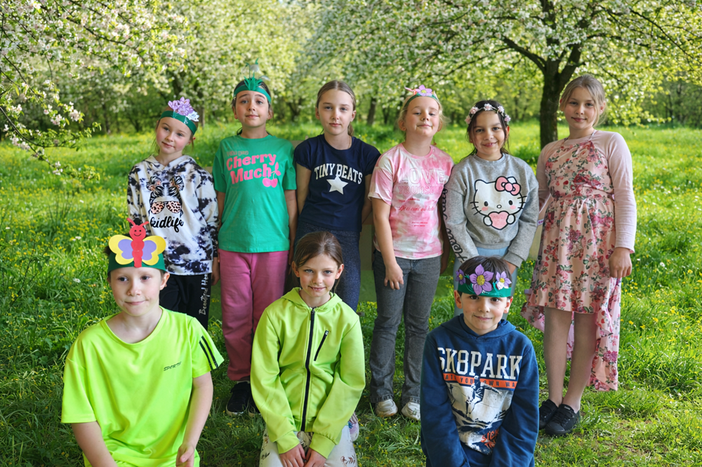 uczniowie w wiosennych strojach na tle kwitnących drzew