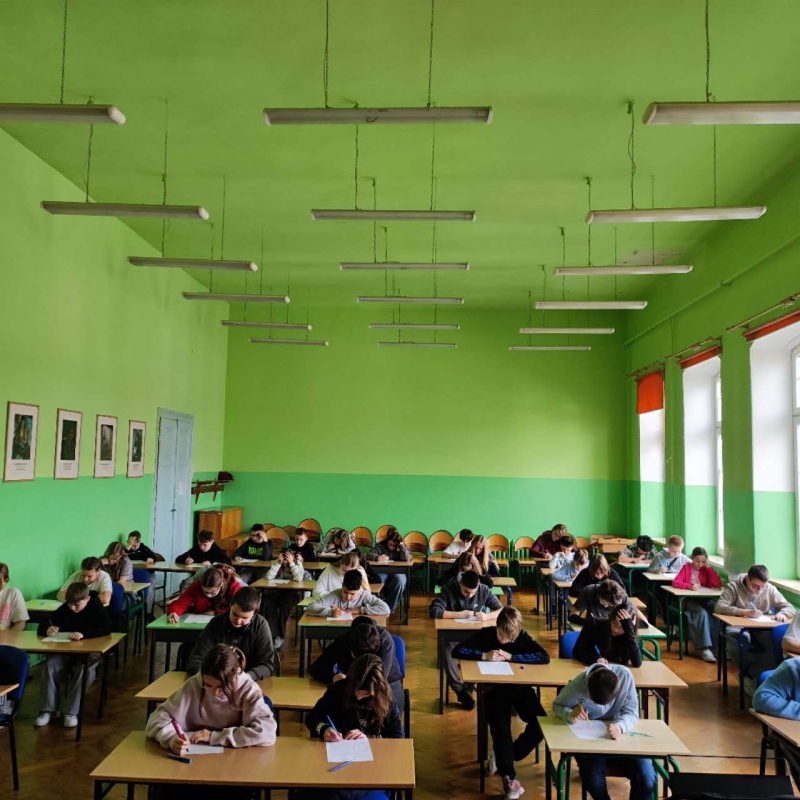 uczniowie w szkolnej auli piszący pracę konkursową