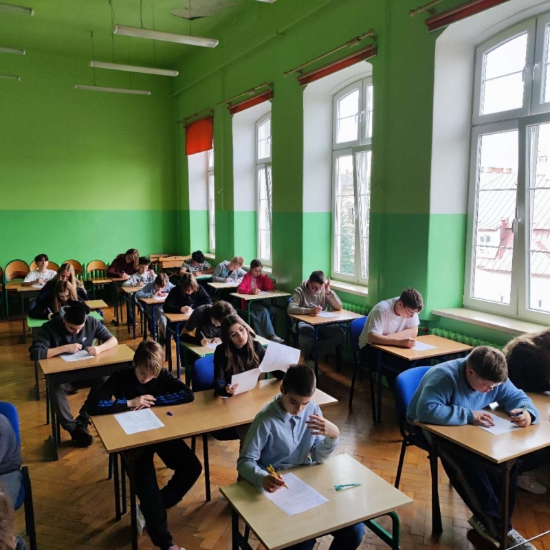 uczniowie w szkolnej auli piszący pracę konkursową