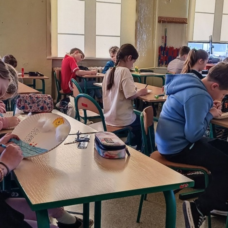 uczniowie w ławkach tworzą pracę plastyczną na papierowych tackach