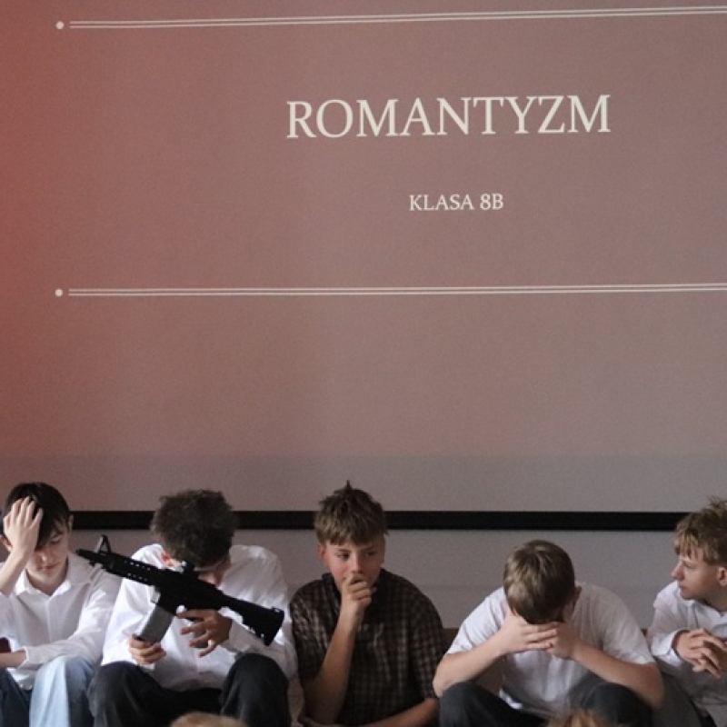 uczniowie siedzą na scenie na tle napisu romantyzm